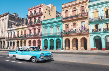 Touristenkarte - Das Visum für Kuba - Oldtimer fährt vor der farbenprächtigen Häuserfront in Kuba vorbei